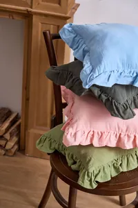 Stack of colorful French ruffle edge pillowcases on a wooden chair by a fireplace