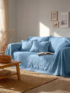 Copridivano in cotone lavato azzurro drappeggiato in un soggiorno luminoso e accogliente
