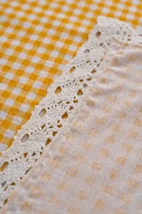 Macro detail of yellow and white gingham tablecloth with decorative floral lace edge