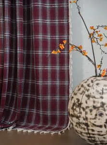 Detailed view of a burgundy plaid wool curtain with decorative white tassel trim