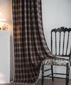 Close-up of brown plaid French curtain with white tassel fringe draping over a black chair