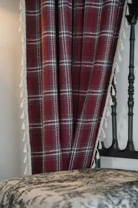 Macro detail of red plaid Christmas curtain with elegant white tassel fringe accents.