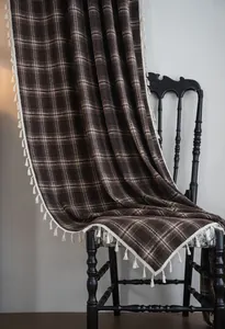 Detail view of coffee plaid French curtain with white tassel fringe on a vintage chair
