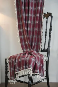 Detail of burgundy plaid wool curtain with white fringe draped over a black chair