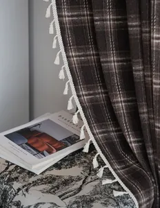 Close-up of brown plaid French curtain featuring delicate white tassel trim detail.