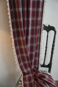 Close-up of elegant burgundy plaid curtain with delicate white tassel trim on a chair.