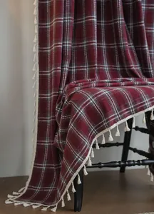 Close-up of a red and white plaid wool curtain with decorative cream tassels.