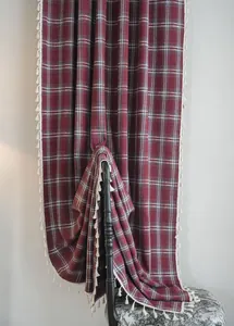 Close-up detail of red plaid wool-like curtain with elegant white tassel fringe edges.