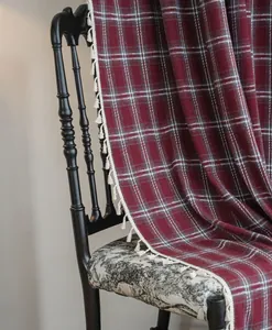 Close-up of red plaid wool curtain featuring white tassel fringe details.