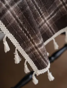 Close-up detail showing the fine texture of brown plaid fabric with white decorative tassels