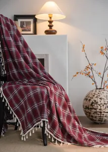 Detail of a red plaid woolen curtain with white tassels draped elegantly over a black chair
