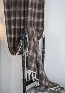 Detail showing texture of a coffee plaid curtain with white tassels draped on a black chair