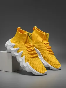 Detail shot of yellow breathable fly-knit high-top sneakers with white wavy chunky soles.