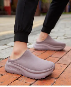 Close-up of a person wearing purple knit thick-sole mule sneakers on a brick path