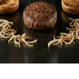 Perfectly round hamburger patty grilling on a flat top with onions and toasted buns.