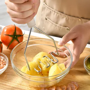 Handmatige roestvrijstalen aardappelstamper die gekookte aardappelen in een glazen kom perst.