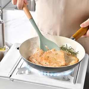 Green silicone spatula with wooden handle used for cooking food in a frying pan on stove