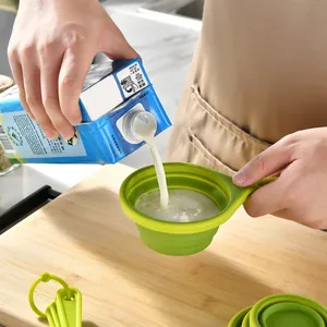 Green silicone collapsible measuring cup used for pouring milk on a wooden board.
