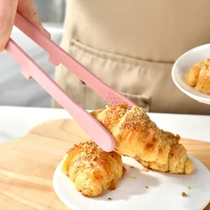 Pink integrated silicone food tongs picking up a fresh croissant in a cozy kitchen setting