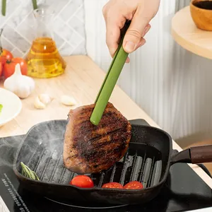 Heat-resistant green silicone kitchen tongs flipping a juicy grilled steak in a pan
