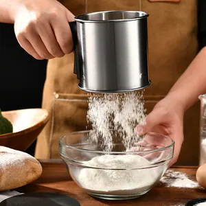 Handheld stainless steel flour sifter sifting flour into a clear glass baking bowl