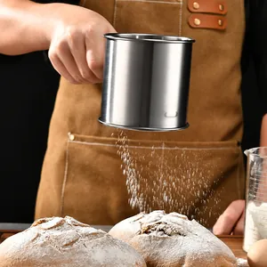 Stainless steel handheld flour sifter sifting powder onto rustic bread loaves