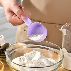 Purple stainless steel measuring cup scooping flour into glass bowl for baking.