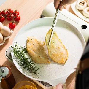 Pince de cuisine en inox retournant du poulet dans une poêle blanche