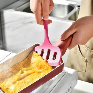 Pink silicone slotted spatula flipping an omelet in a non-stick frying pan for cooking