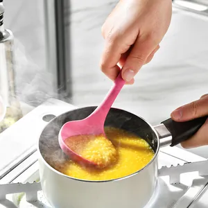 Heat resistant pink silicone soup ladle stirring porridge in a white pot on stove