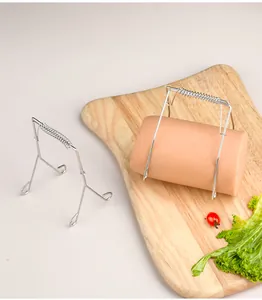 Stainless steel spring clip holding a large sausage on a wooden cutting board