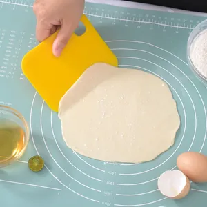 Yellow plastic dough scraper tool for baking bread and pastry on a silicone mat with flour