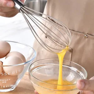 Gros plan d'un fouet en acier inoxydable battant des œufs dans un bol en verre de cuisine