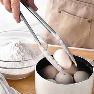 Pince de cuisine en silicone et inox saisissant un œuf bouilli dans une casserole d'eau