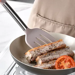 Gros plan d'une spatule fendue en silicone avec manche en inox faisant frire du porc