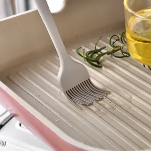Détail d'un pinceau de cuisine en silicone gris appliquant de l'huile dans une poêle.