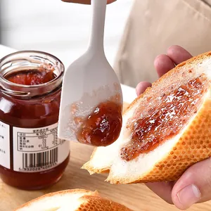 Détail d'une spatule en silicone blanc étalant de la confiture sur une tranche de pain