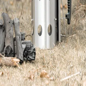 Close-up of stainless steel charcoal chimney starter in outdoor BBQ setting on dry grass.