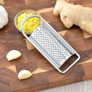 Manual stainless steel ginger and garlic grater tool shown on a rustic wooden cutting board