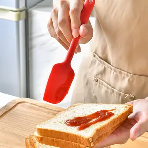 Professional red silicone baking spatula spreading delicious jam on fresh bread slice