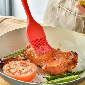 Heat-resistant red silicone basting brush for oiling meat and vegetables in a pan