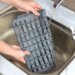 Gray PVC non-slip kitchen sink draining mat being washed under running water in a sink
