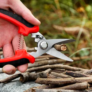 Sécateur de jardin rouge ergonomique coupant une branche dans un décor de jardin.