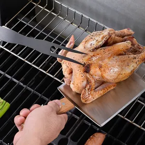 Professional wood handle griddle spatula and BBQ fork lifting a roasted chicken