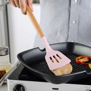 Pink silicone spatula with wooden handle flipping chicken breast in grill pan