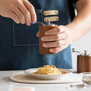 Portable wooden manual hand-crank spice and coffee grinder mill shown grinding over pasta