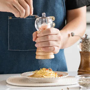 Manual wood and acrylic pepper grinder being used to season a plate of pasta with spices