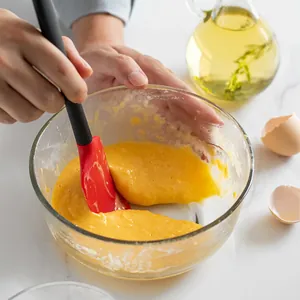 Professional red silicone baking spatula mixing cake batter in a clear glass bowl scene.