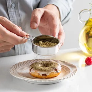Professional stainless steel flour sifter for baking shown sifting powder onto a delicious donut