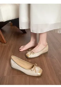 Primo piano di eleganti ballerine dorate con fiocco su un pavimento in legno